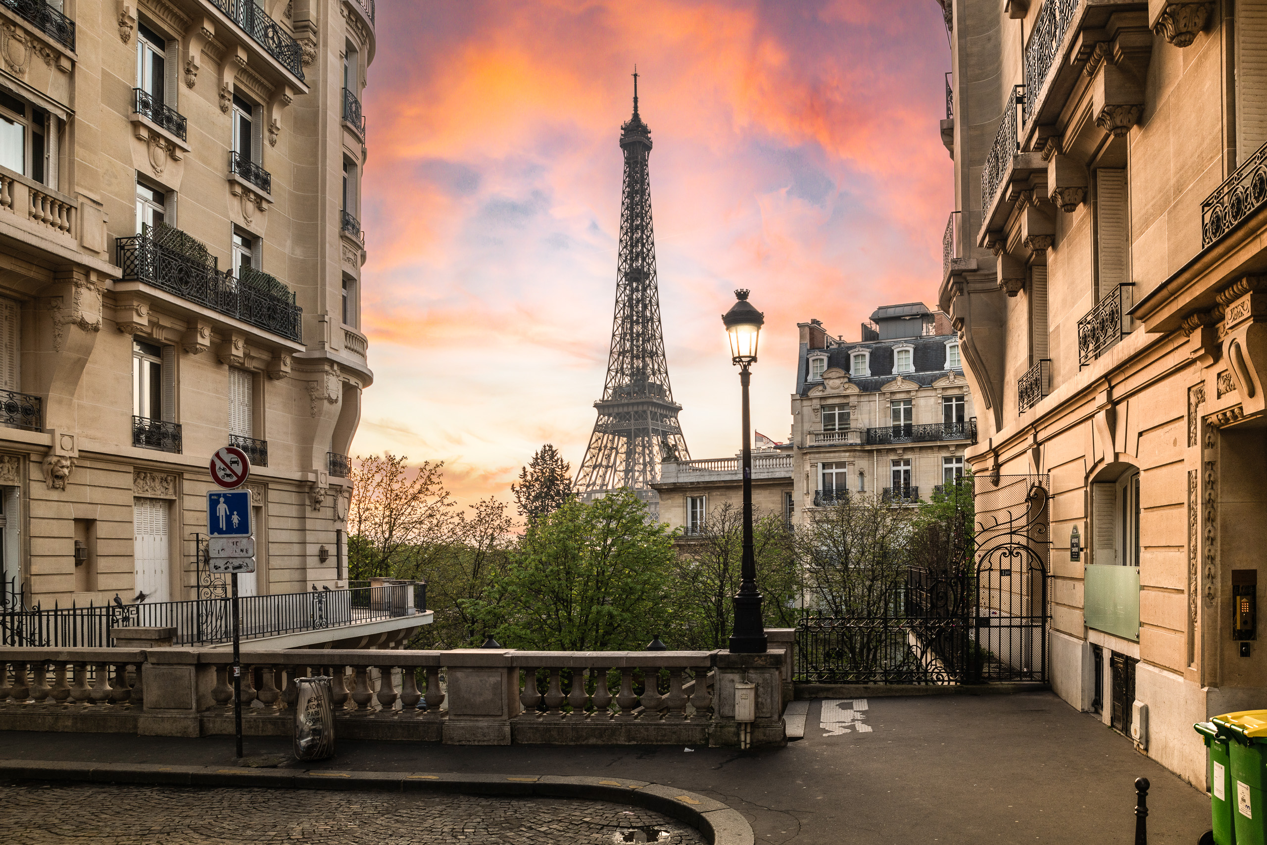 Sunrise photograph of the Eiffel Tower viewed from Avenue de Camoëns in Paris with soft pastel sky and classic Parisian buildings