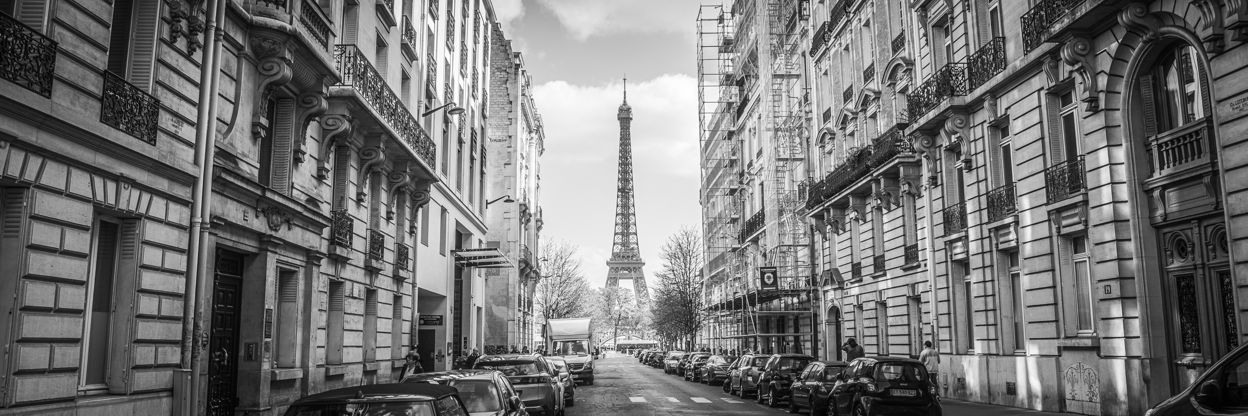 Black and white panoramic photograph of a Paris street framing the Eiffel Tower between classic Haussmann buildings