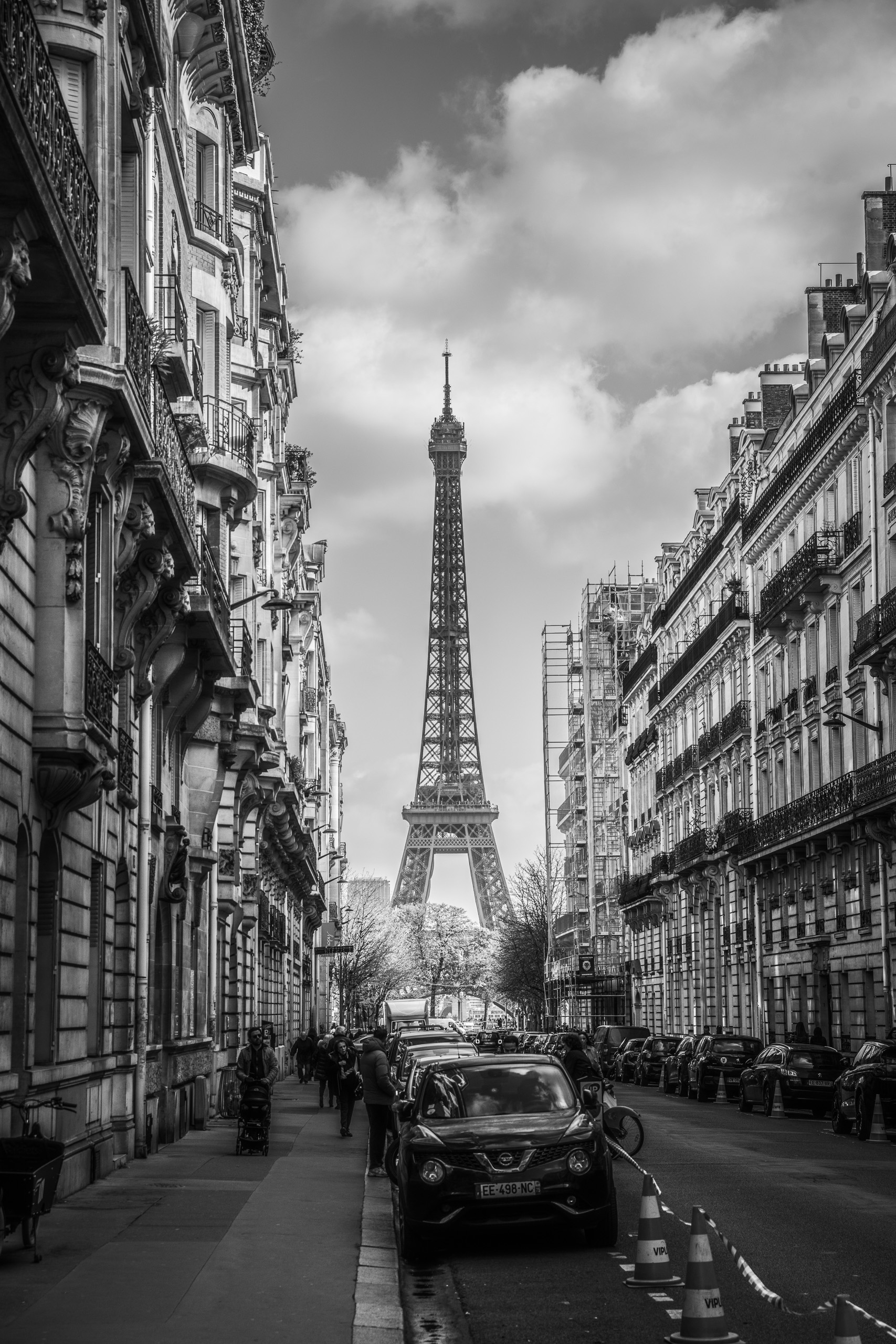 Black and white photo of the Eiffel Tower framed by Parisian buildings on a city street