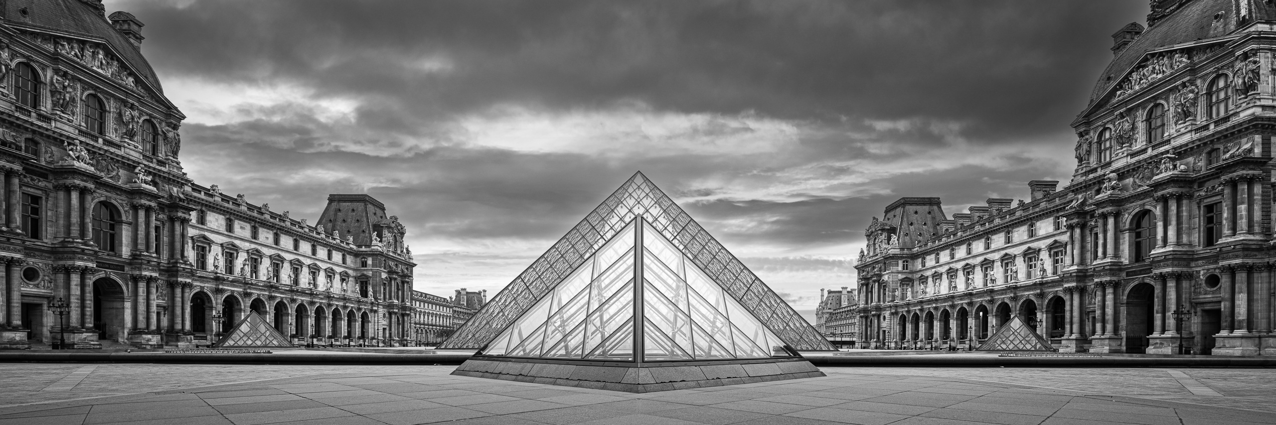 Black and white panoramic photograph of the Louvre Pyramid framed by the historic Louvre Palace in Paris