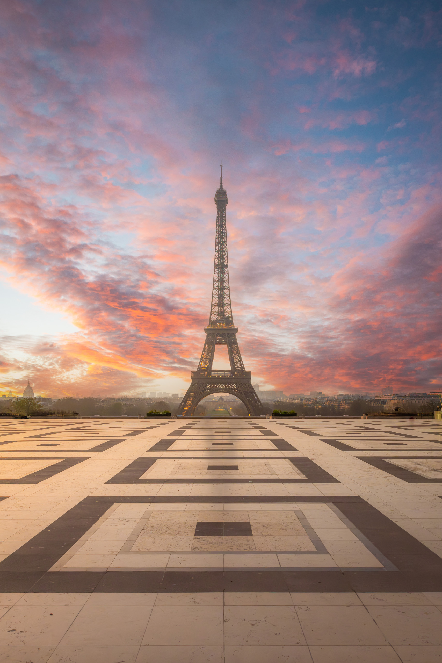 Vertical sunrise photograph of the Eiffel Tower rising above the Trocadéro Plaza beneath pastel pink and blue morning clouds in Paris