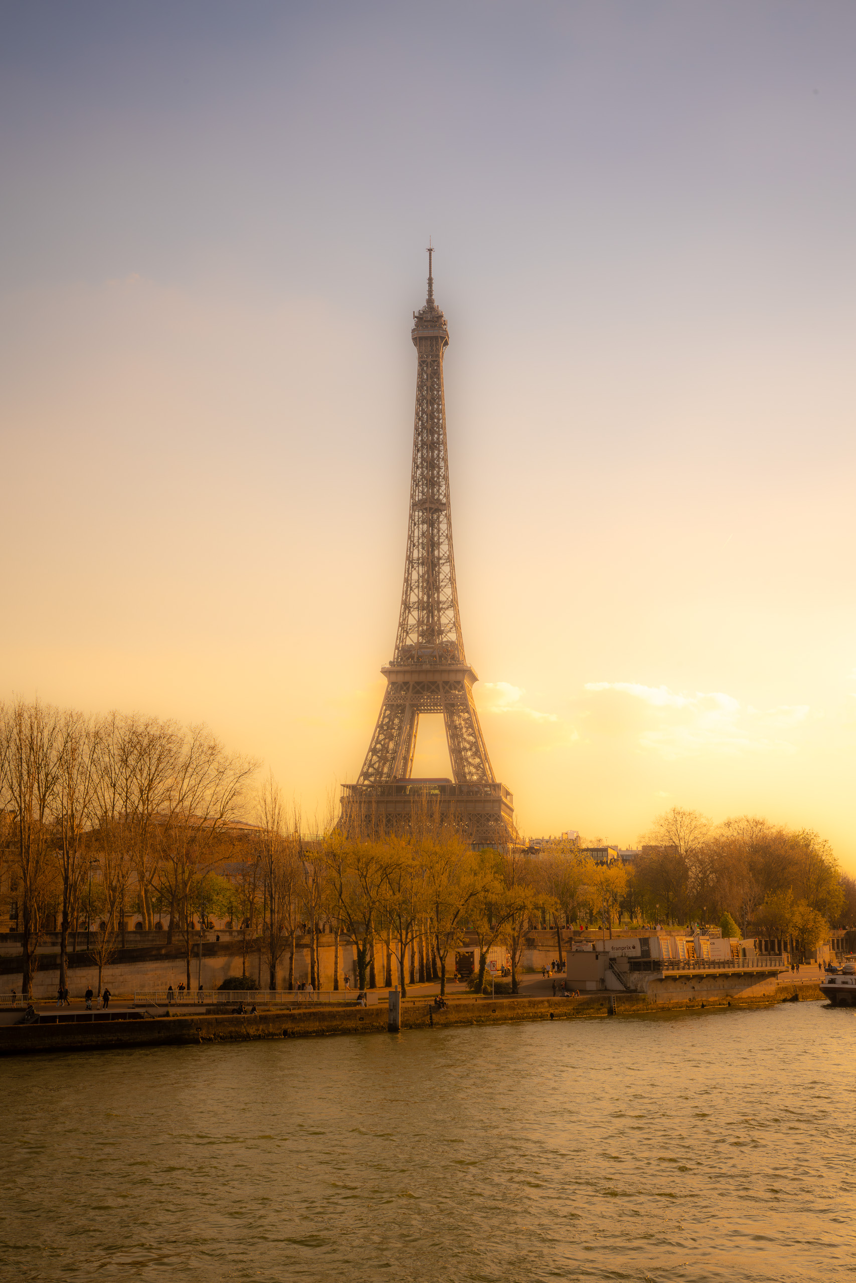 Sunrise photograph of the Eiffel Tower along the Seine River in Paris with soft golden morning light and calm reflections
