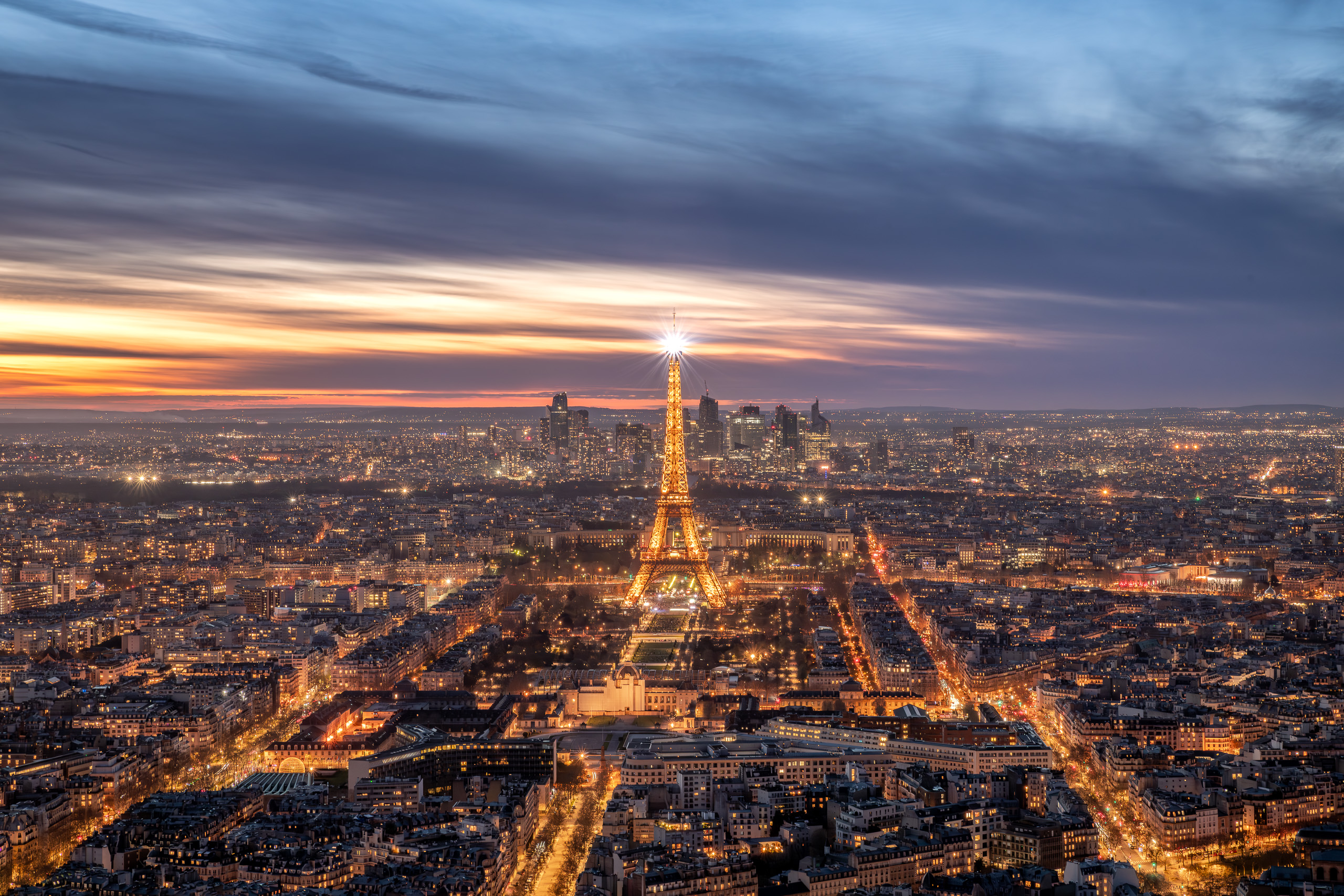 Sunset photograph of the Eiffel Tower illuminated at night overlooking the Paris city skyline with glowing streets and dramatic evening sky