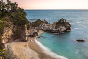 McWay Falls in Big Sur California flowing onto sandy beach with turquoise ocean and rocky coastline