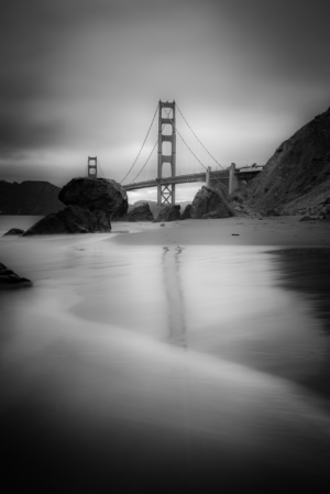 Black and white Golden Gate Bridge view from beach with rocks and reflection in San Francisco