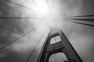 Black and white upward view of Golden Gate Bridge cables and tower fading into fog in San Francisco