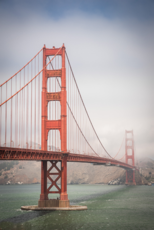 Vertical photograph of the Golden Gate Bridge in San Francisco with fog surrounding the towers and bay water below