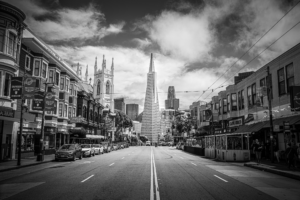 Black and white view of San Francisco street leading to the Transamerica Pyramid with city buildings and dramatic clouds
