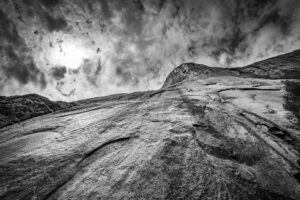 Black and white upward view of El Capitan in Yosemite showing granite wall and dramatic clouds above