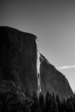 Black and white vertical photograph of El Capitan in Yosemite with Horsetail Fall cascading down the granite face