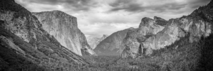 Black and white panoramic view of Yosemite Valley in California with granite cliffs, forest, and dramatic clouds