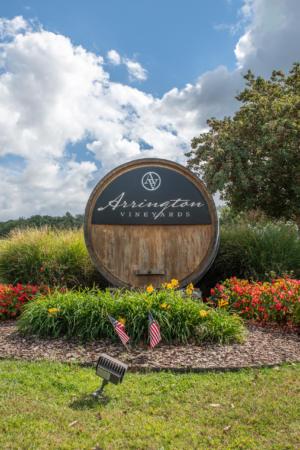 Entrance sign for Arrington Vineyards near Franklin, Tennessee, featuring a large wooden wine barrel surrounded by colorful flowers beneath a bright blue sky.