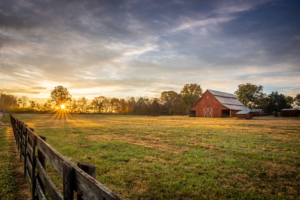 Historic red barn at sunrise near Franklin, Tennessee, with sun rays stretching across a peaceful pasture beneath a colorful morning sky.
