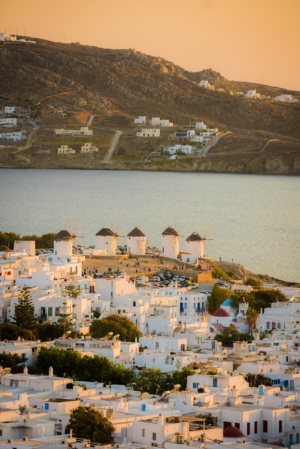 Mykonos Greece at sunset with white hillside buildings overlooking the Aegean Sea in warm golden light