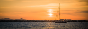 Sailboat at sunset on the water in Naxos Greece with orange sky and mountain silhouettes