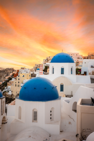 Santorini blue-domed churches at sunset in Oia, Greece, with glowing orange sky and white Cycladic architecture
