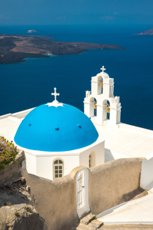 Blue dome church and white bell tower overlooking the sea in Santorini Greece