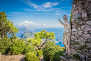 Horizontal photograph of stone statue overlooking Capri Italy coastline and blue Mediterranean Sea