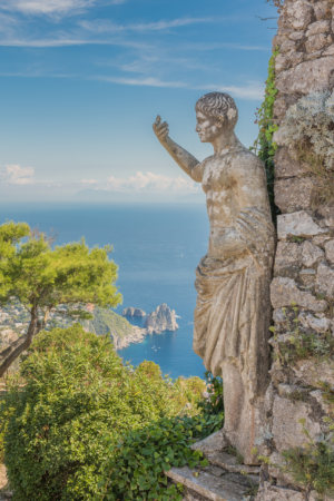 Vertical photograph of stone statue overlooking the sea on Capri Italy with blue sky and coastline