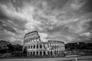 Black and white horizontal photograph of the Colosseum in Rome Italy beneath dramatic storm clouds