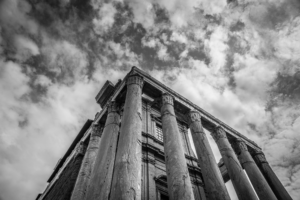 Black and white view of ancient columns at the Roman Forum in Rome Italy beneath dramatic clouds