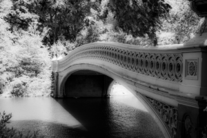 Black and white horizontal view of Bow Bridge in Central Park arching over calm water in New York City
