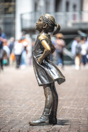 Fearless Girl statue in color standing on cobblestone street in New York City