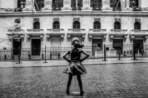 Fearless Girl statue facing Wall Street in black and white horizontal scene in New York City