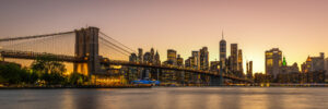Panoramic New York City skyline and Brooklyn Bridge at sunset with Manhattan lights