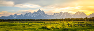 Panoramic sunset view of Grand Teton mountains with meadow and fence in Wyoming