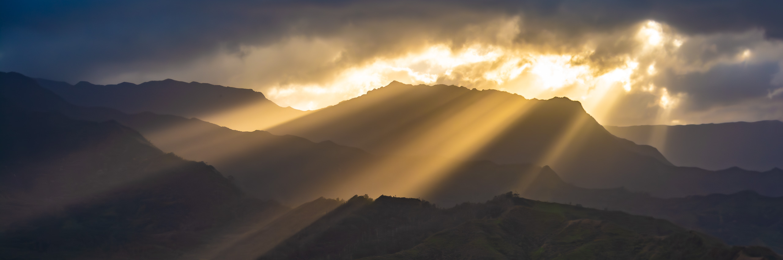 Golden sunset rays shining through clouds over mountain ridges in Kauai Hawaii panoramic landscape