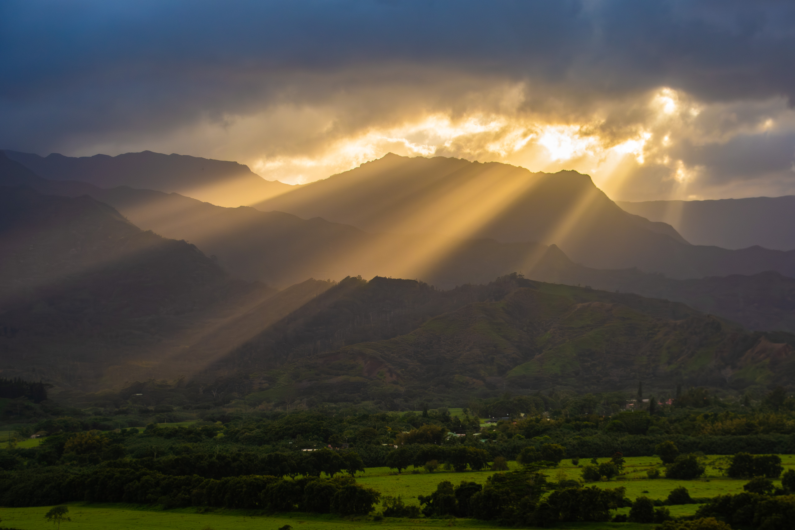 Golden sun rays breaking through clouds over lush mountain landscape in Kauai Hawaii