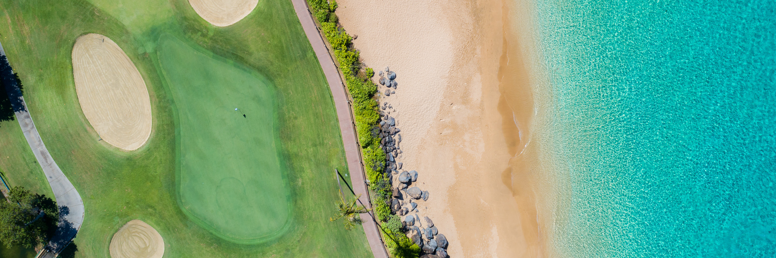 Aerial panorama of Maui Hawaii golf course along tropical beach with turquoise ocean and white sand shoreline