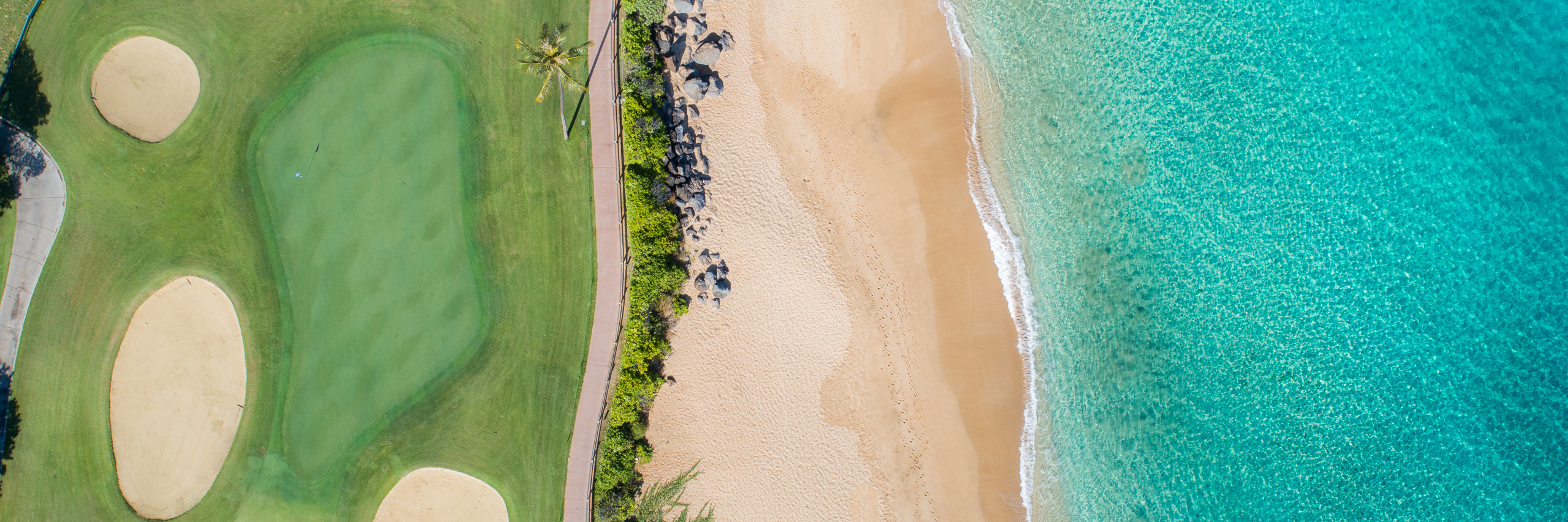 Aerial view of Maui Hawaii golf course beside sandy beach and turquoise ocean water panorama