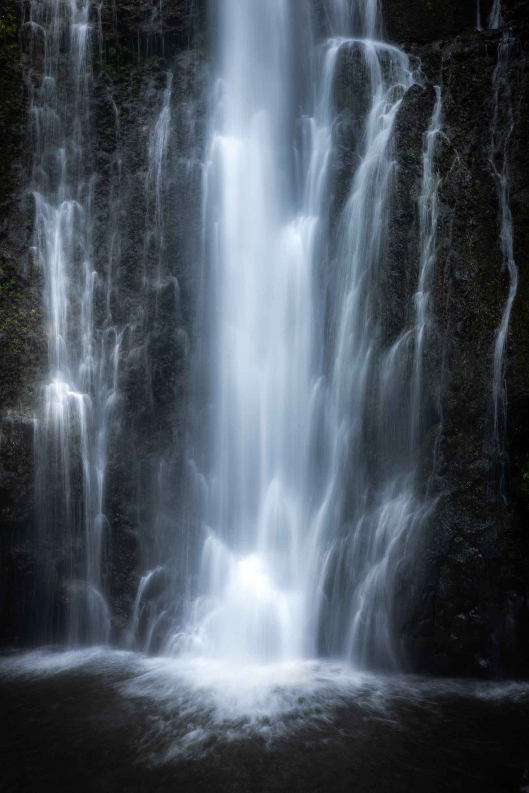 Silky waterfall in Maui Hawaii flowing over dark volcanic cliffs into a misty pool below