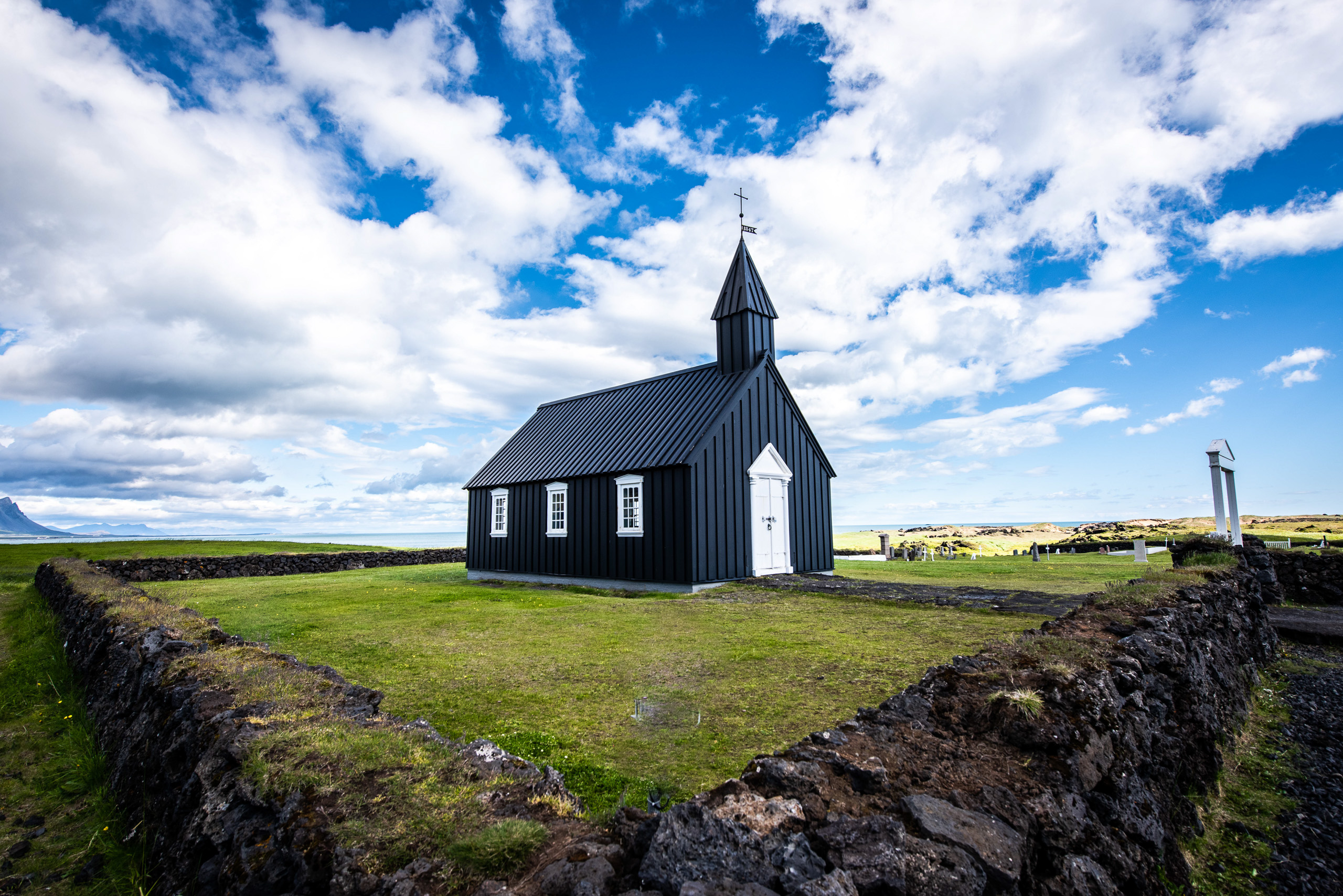 Budir Black Church in Iceland under blue sky with white clouds and green landscape