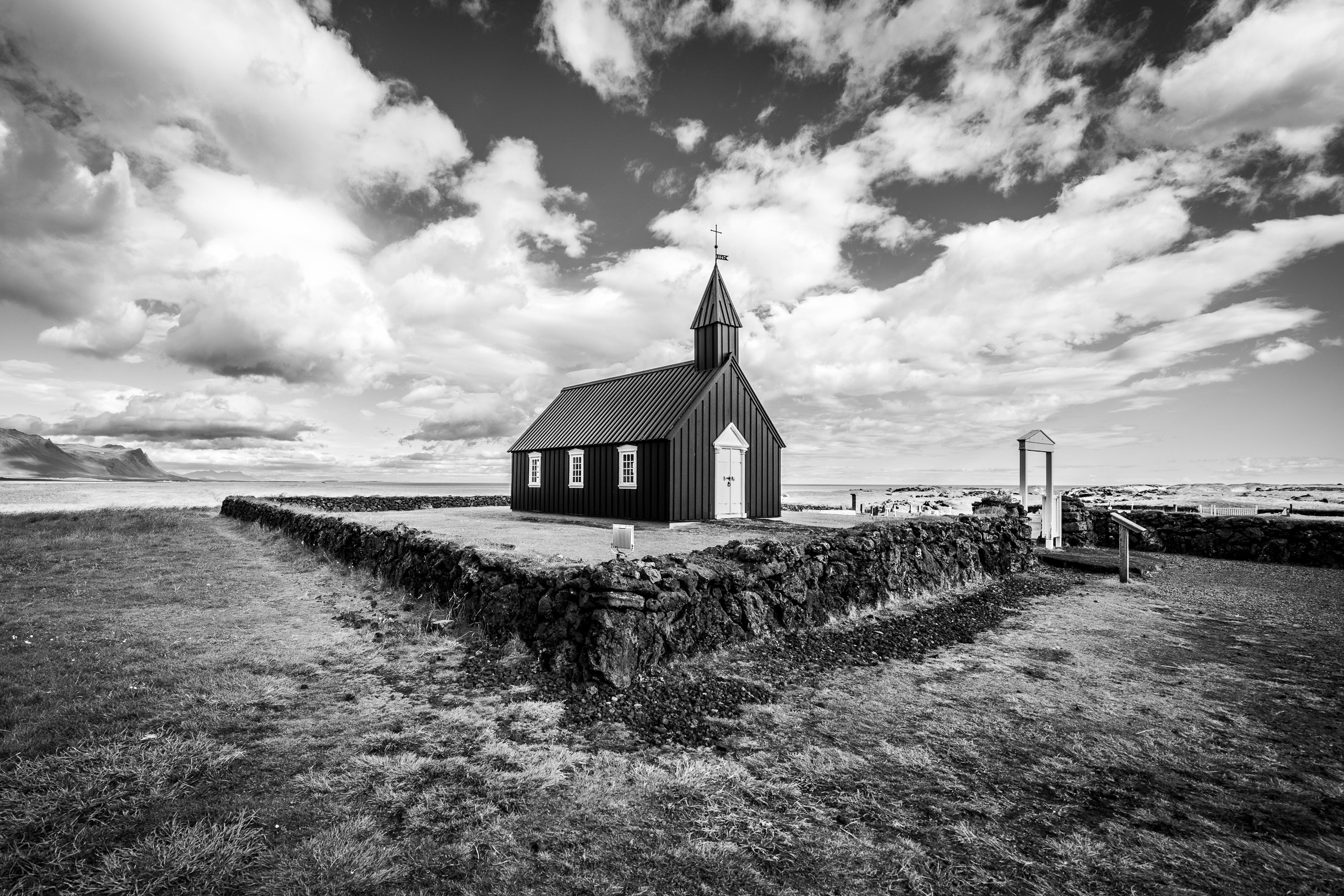 Black and white landscape photo of Budir Black Church in Iceland with clouds and lava stone wall