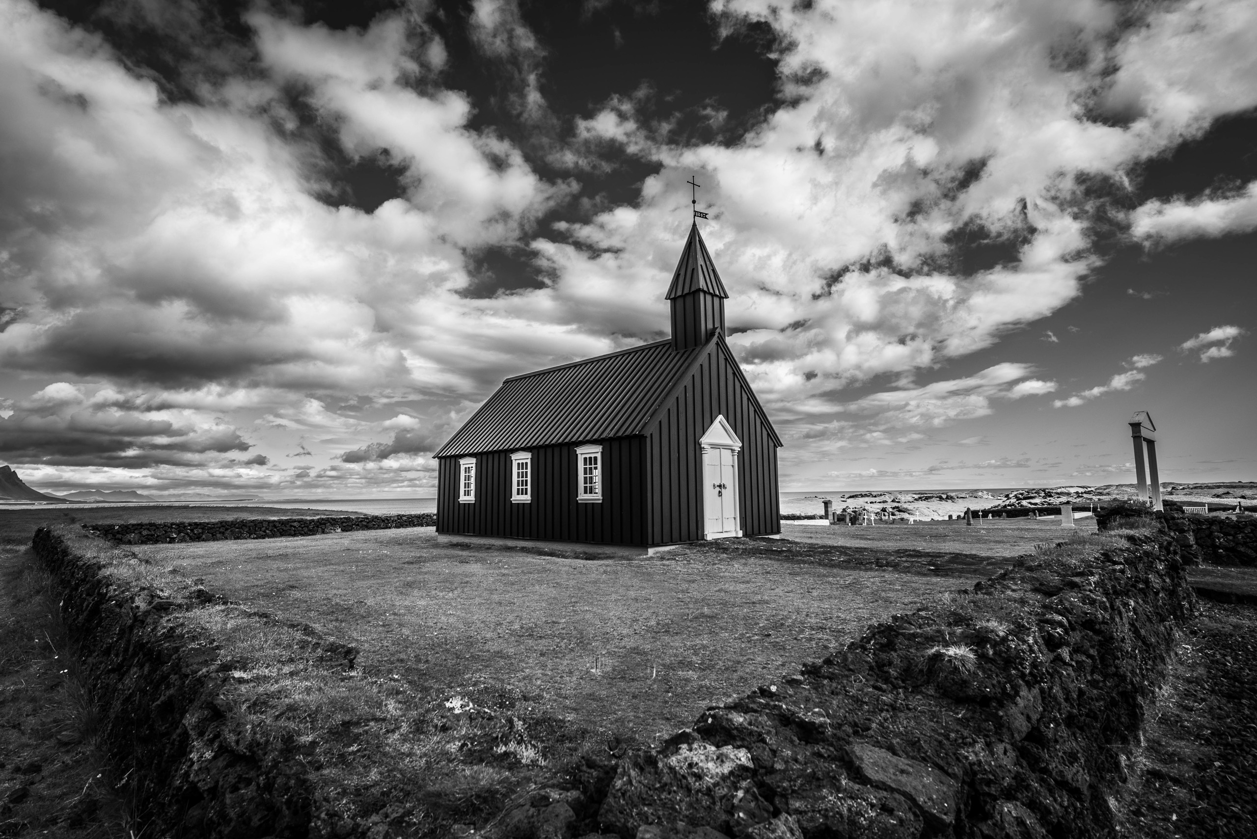 Black and white photo of Budir Black Church in Iceland beneath dramatic clouds