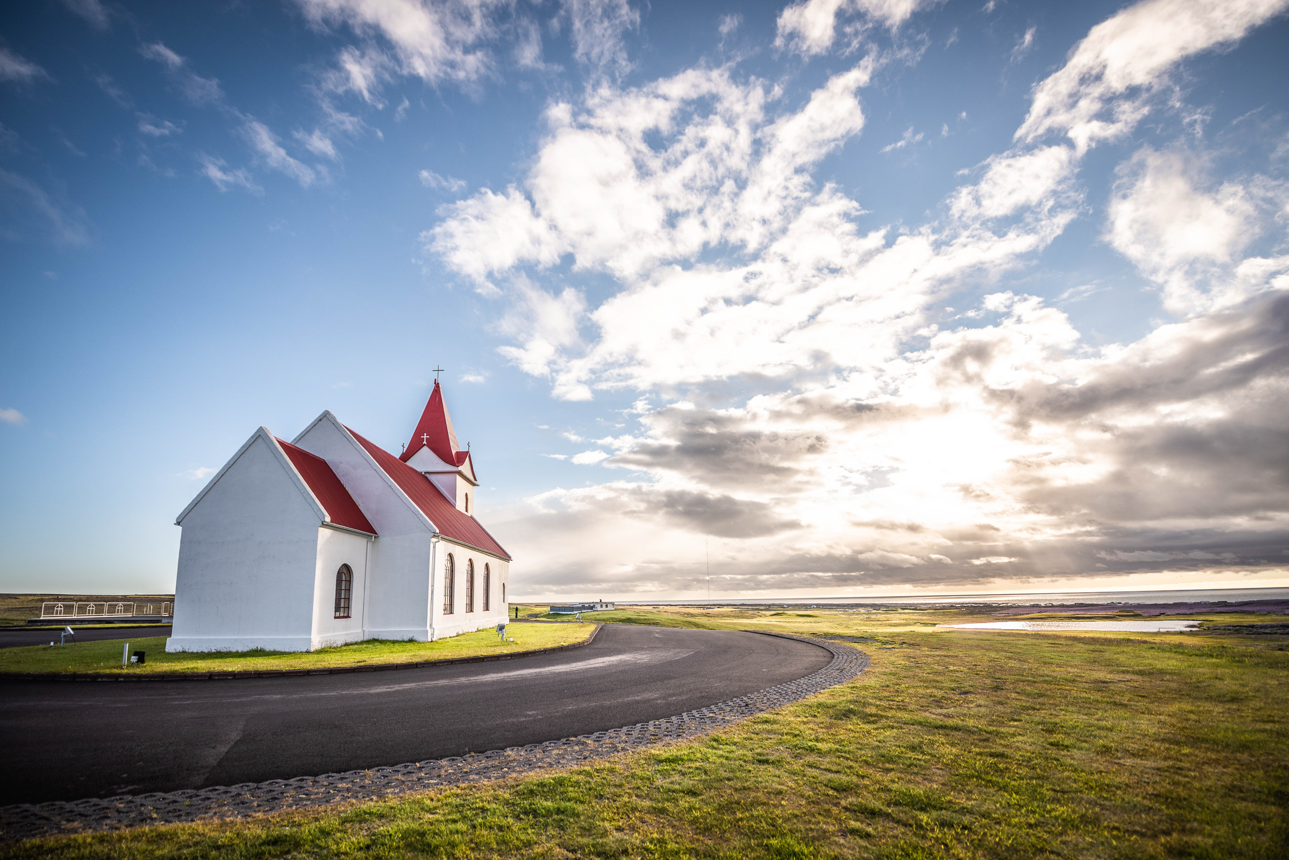White church with red roof in Iceland beside curved road at sunset under dramatic clouds