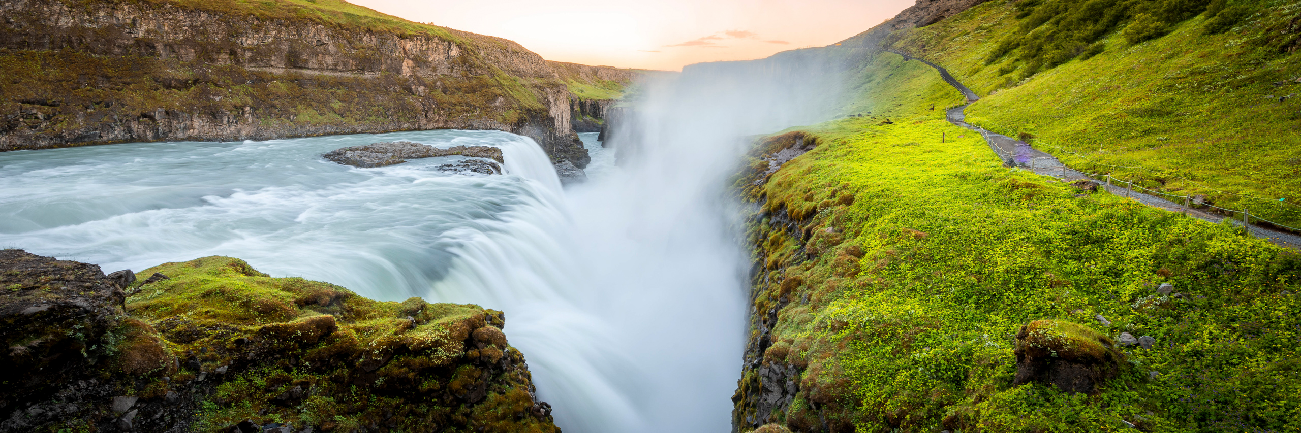 Panoramic photograph of Gullfoss waterfall in Iceland cascading through a dramatic green canyon