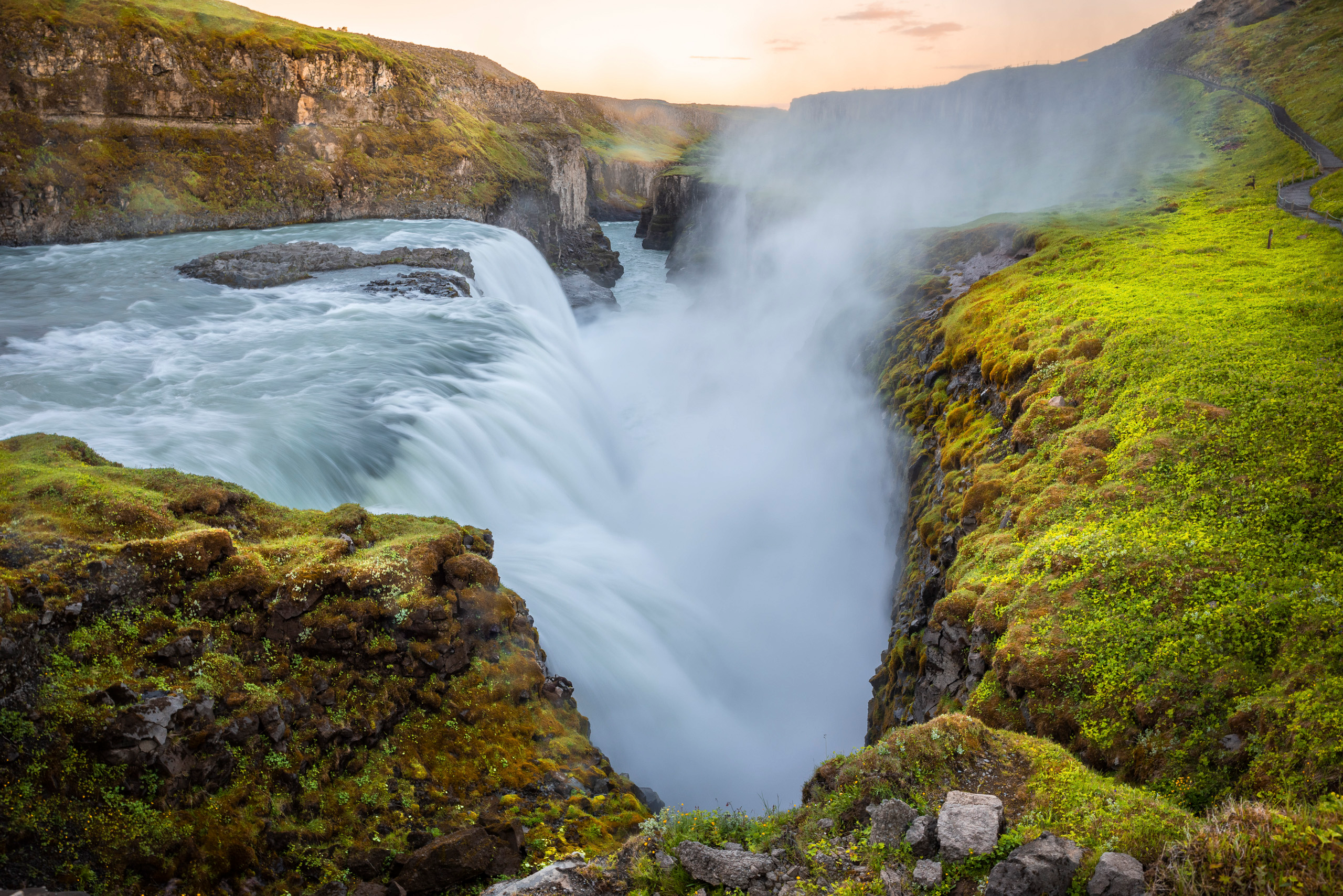 Powerful Gullfoss waterfall plunging into canyon surrounded by green landscape in Iceland