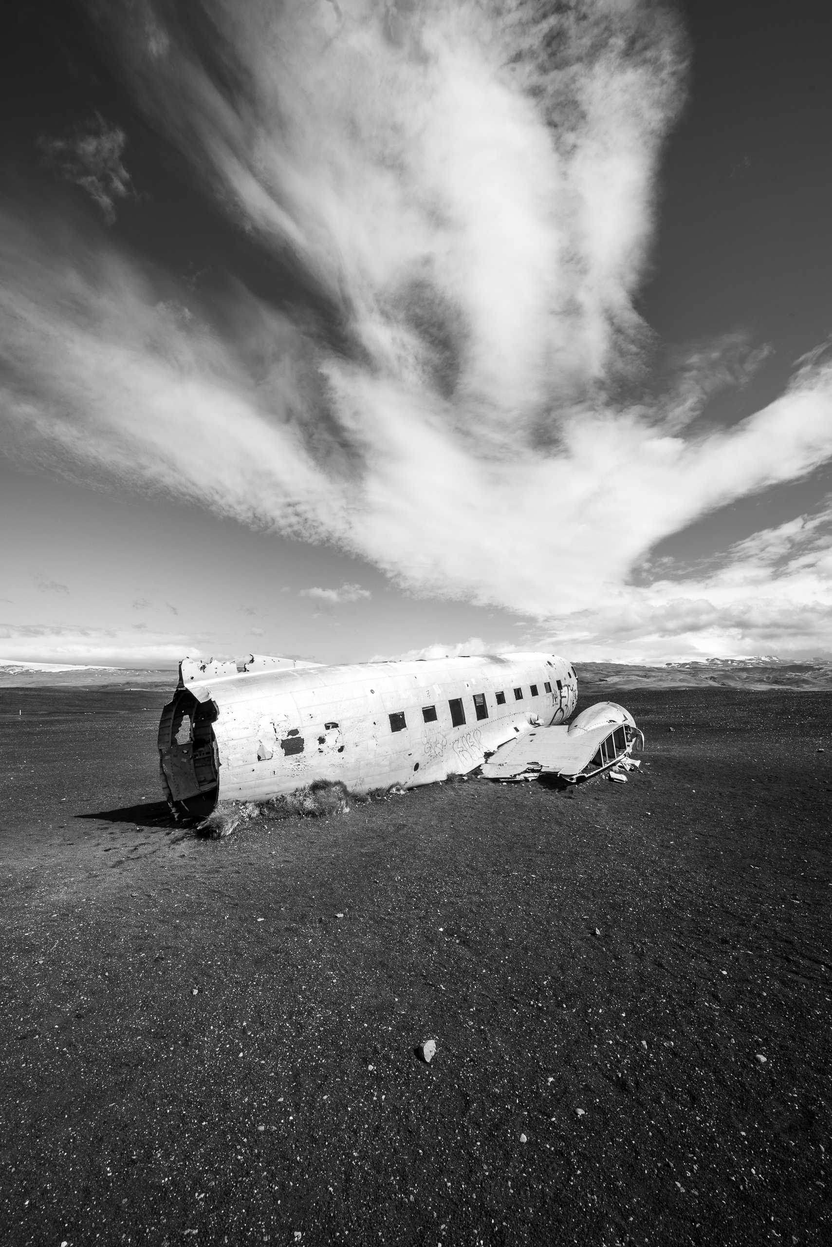 Black and white photo of abandoned plane wreck on black sand beach in Iceland under dramatic clouds