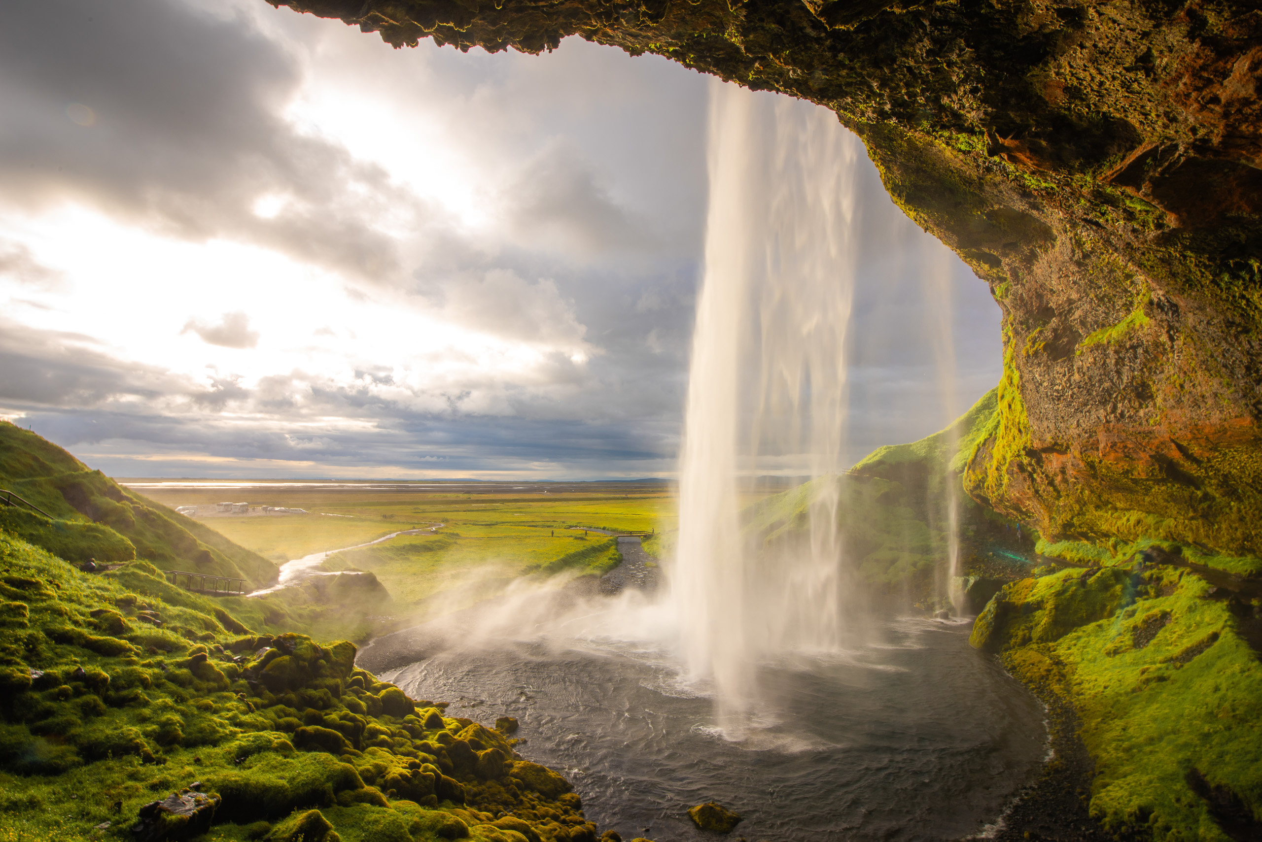 Seljalandsfoss waterfall in Iceland viewed from behind with moss covered cliffs and sunlight