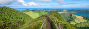 Wide panoramic photograph of Sete Cidades in the Azores with a ridge trail, green mountains, and blue Atlantic Ocean