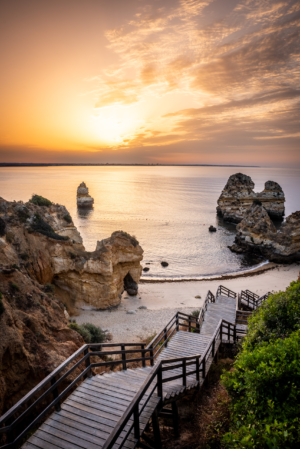 Sunrise over Camilo Beach cliffs and wooden stairs in Algarve Portugal