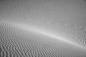 Black-and-white abstract photograph of wind-sculpted gypsum sand ripples at White Sands National Park, revealing intricate textures and flowing natural patterns.