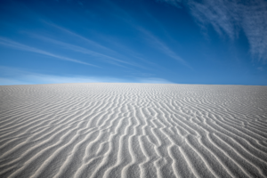 Brilliant white gypsum sand ripples stretch across White Sands National Park beneath a deep blue sky filled with wispy desert clouds.