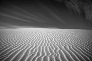 Black-and-white panorama of intricate gypsum sand ripples at White Sands National Park, stretching endlessly beneath dramatic desert clouds and a darkened sky.