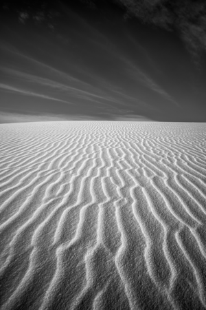 Black-and-white photograph of intricate gypsum sand ripples at White Sands National Park, where repeating patterns stretch toward the horizon beneath dramatic desert skies.