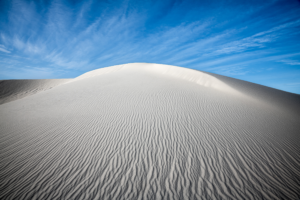 Brilliant white gypsum dune rises beneath a deep blue sky at White Sands National Park, with intricate ripple patterns leading toward the sunlit crest.